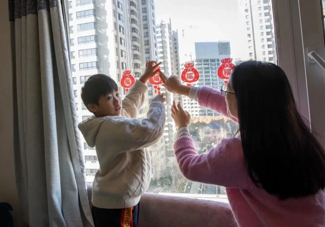 馨逸公寓的谈晓燕和儿子一起在家里的窗户上贴春节贴纸